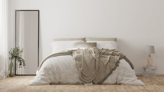 Neutral bedroom with a cosy bed, soft throw blanket, full-length mirror, bedside lamp, and wooden flooring.