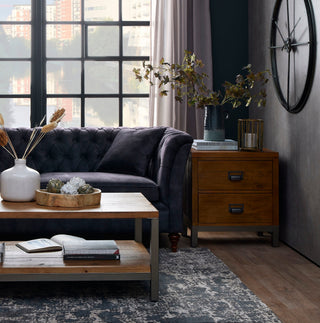 Cosy living room with grey chesterfield sofa, wooden coffee table, black framed windows and natural light.