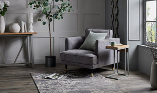 Grey armchair with a side table in a modern living space with panelled walls and soft natural lighting.