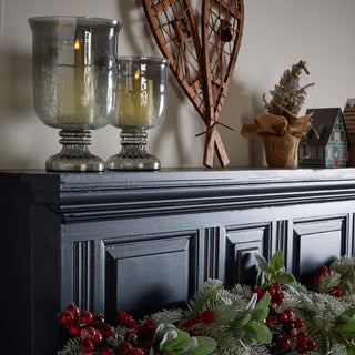 A decorated fireplace mantel featuring a green wreath and a lit candle, creating a warm and inviting atmosphere.