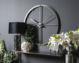 A black wall clock with a white flower vase placed in front of it, creating a contrasting and elegant display.