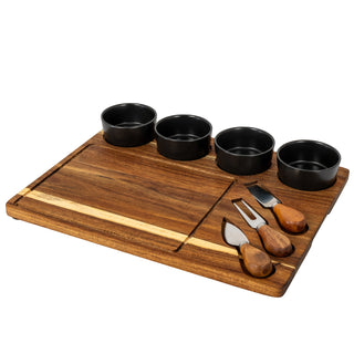 Angled view of the acacia board with four grey bowls and three knives in their cutouts.