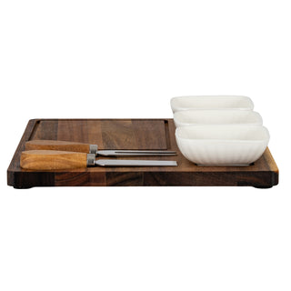 Two wooden-handled cheese tools and three stacked white ceramic bowls resting on the acacia serving board.