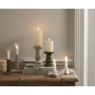 Styled scene showing the cream fluted pillar holder alongside green and white ceramic candle holders on a wooden table.