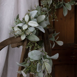Close up of the soft green foliage and white berries draped over a rustic wooden frame.
