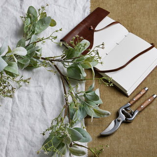 Artificial foliage and white berries laid flat with secateurs and a brown leather journal.