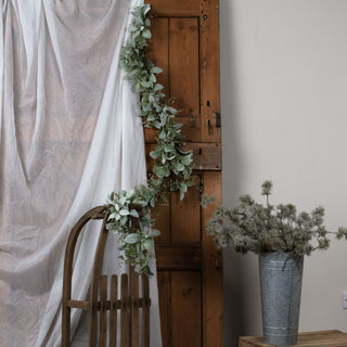 Garland draped over a rustic wooden door and a wooden sledge, next to a sheer white curtain.