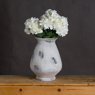 Vase filled with white hydrangeas, displayed on a rustic wooden table against a dark wall.