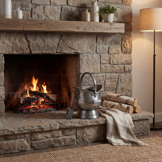 Antique pewter coal bucket and shovel on a stone hearth next to a burning fire.
