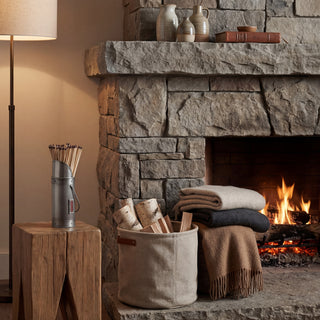 Pewter match holder on a rustic wooden stool next to a lit stone fireplace. Long matches are visible.