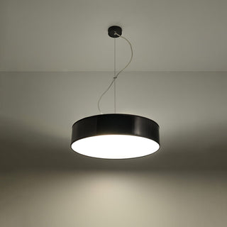 Angled view of the black pendant lamp illuminated, showing the bright downward light cast onto the wall.