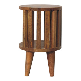 Front view of the round wooden bedside table showing the open slatted sides, internal shelf, and three tapered legs.