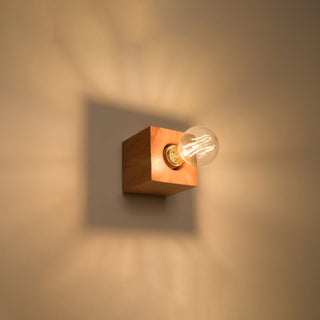 Natural wood wall light illuminated, creating a square shadow and warm light on the wall.