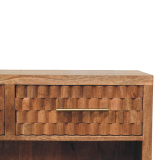 Brass bar handle against the carved golden teak drawer front, showing the wood grain texture.