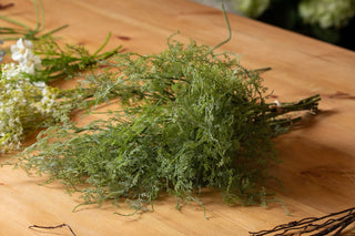 Artificial asparagus fern bunch lying flat on a wooden surface, showing the dense foliage and tied stems.