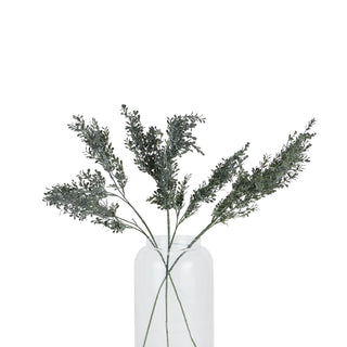 Multiple artificial blackened grass stems arranged in a clear glass vase on a white background.
