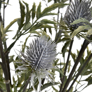 Close detail of two artificial blue thistle heads and serrated green foliage against a white background.