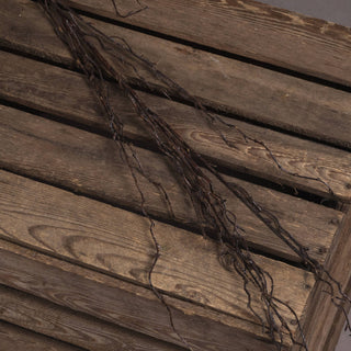 Close detail of the thin, dark artificial branch spray lying across rustic wooden slats.