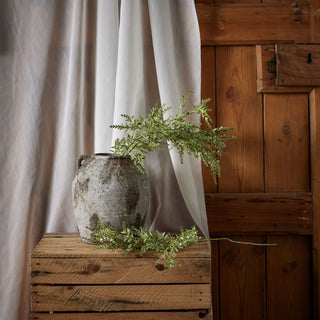 Broom stem arranged in a distressed vase on a wooden crate.