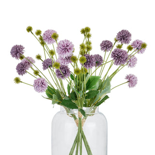 Artificial purple chrysanthemum bouquet displayed upright in a clear glass vase against a white background.
