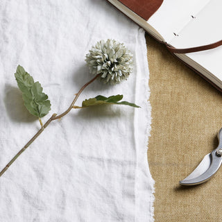 Detail of the pale green blue artificial chrysanthemum flower and leaves, styled on white linen and jute.
