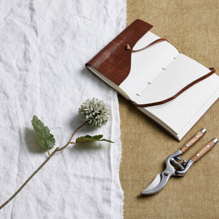 Pale green blue artificial chrysanthemum stem displayed with gardening tools and a brown leather journal.