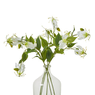 Artificial cream Gloriosa stems and foliage arranged in a clear glass bottle against a white background.