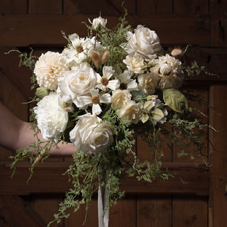 Artificial dahlia bloom featured in a mixed bouquet of white flowers and trailing greenery, held against a dark wood panel background.