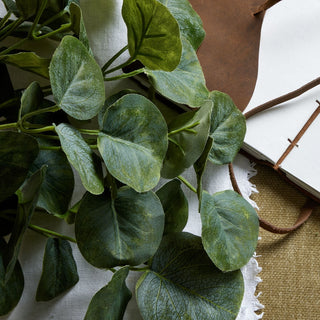 Textured artificial eucalyptus leaves against a white cloth and brown leather journal.