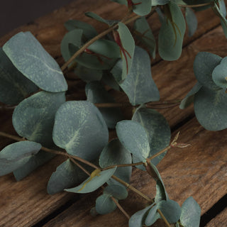 Close-up detail of the artificial eucalyptus stem showing branching structure and new leaf buds on rustic wood.