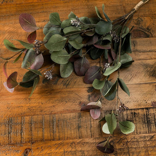 Variegated artificial eucalyptus bouquet featuring green and reddish foliage, displayed on rustic wood.