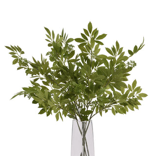 Artificial fennel stems bunched together in a clear square vase on a white background.