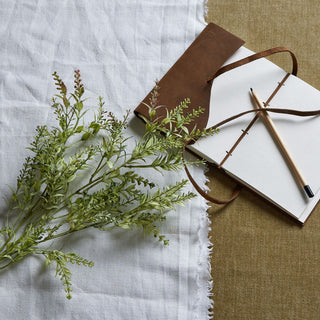 The artificial broom stem is laid diagonally across a white cloth next to a brown notebook and pencil.