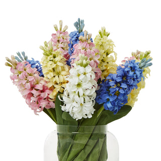 Artificial hyacinth stems in blue, pink, yellow, and white, grouped in a clear glass vase against a white backdrop.