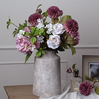 Mixed floral arrangement in a tall textured grey vase on a wooden surface in a home setting.