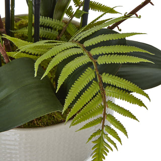 Detail shot showing the bright green artificial fern frond extending over the edge of the light grey ceramic pot.