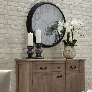 Artificial orchid in a stone pot displayed on a wooden sideboard next to candlesticks, against a white brick wall.