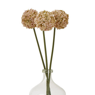 Three artificial pink allium stems displayed in a clear glass bottle vase on a white background.