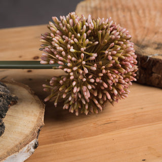 Close detail of the artificial pink allium flower head buds on a light wooden surface with bark sections.