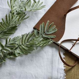 Close up of the flocked, grey-green artificial wattle leaves on white fabric.