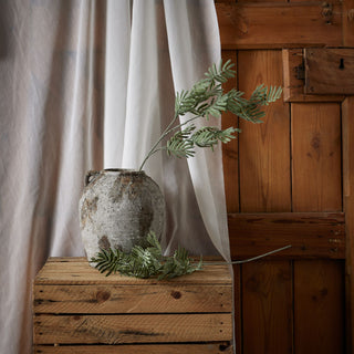 Artificial silver wattle stem arranged in a textured grey pot on rustic wooden crates.