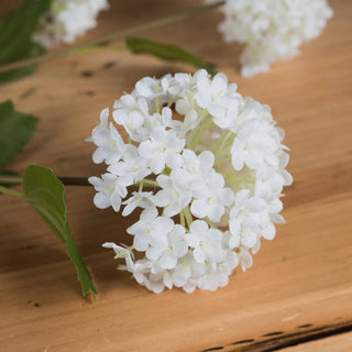 Close-up view of the spherical white artificial viburnum flower resting on a light wood surface.