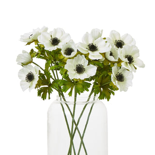 Artificial white anemone stems displayed as a bouquet in a clear glass vase.