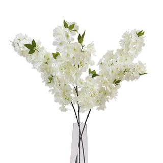 Artificial white cherry blossom stems displayed in a clear glass vase on a plain white background.
