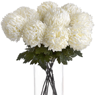 Dense bouquet of artificial white chrysanthemums and foliage in a clear cylindrical vase.