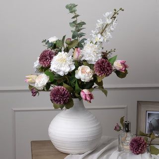 White delphinium stem providing height in a large mixed floral arrangement displayed in a round white vase.