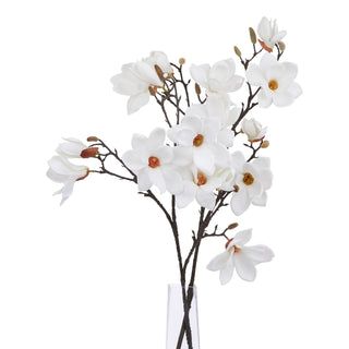 Artificial white magnolia stem displayed upright in a narrow clear glass vase against a plain white background.