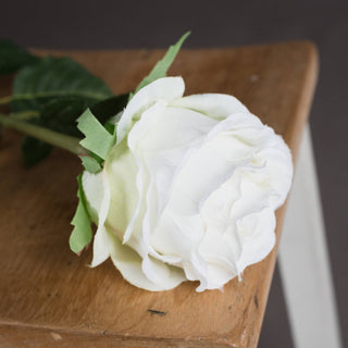 Detail shot showing the layered white petals of the artificial rose head on distressed wood.