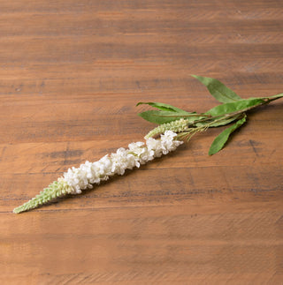 Artificial white veronica floral stem with green leaves, lying on a rustic wooden surface.