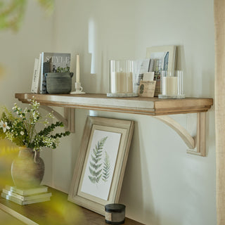 Two glass hurricane lanterns with stone bases displayed on a wooden shelf with books and decor.